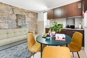 A modern living room with a stone wall, a sofa, and a round table with chairs. - GuestReady - Courtyar 9/99 - Apt 05 (Porto)