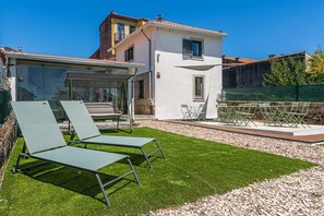 Eine moderne Villa mit Terrasse, zwei Liegestühlen, einem Tisch und einem kleinen Garten.