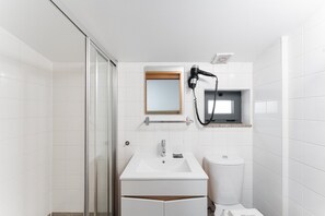 Ein Badezimmer mit Duschkabine aus Glas, einem weißen Waschbecken, einem Spiegel und einem an der Wand montierten Föhn.