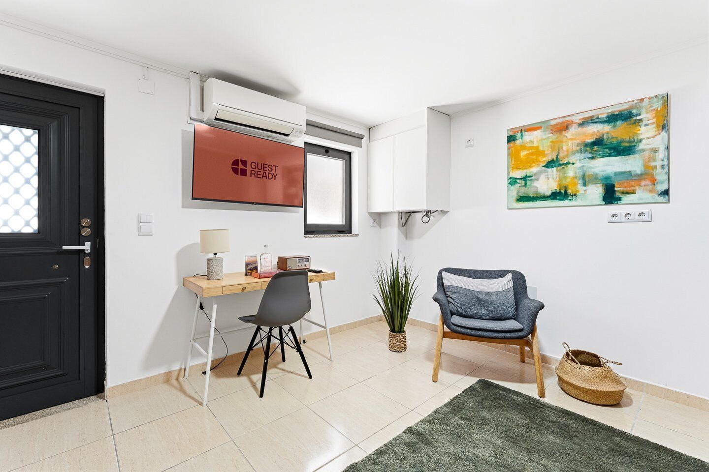 Una habitación de hotel con escritorio, silla, aire acondicionado, una obra de arte y una puerta.