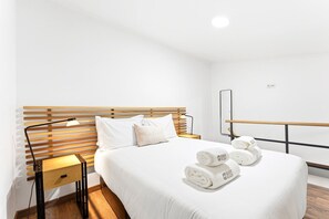 Ein Hotelzimmer mit Holz-Kopfteil, einem Bett mit weißer Bettwäsche, einem Nachttisch mit Lampe und einem Handtuchhalter mit Handtüchern.