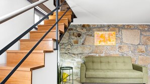 Eine Treppe mit Holzstufen und schwarzen Geländern, ein grünes Sofa, eine Steinwand und ein Gemälde.