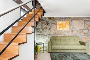 A staircase with wooden steps and black railings, a green sofa, a stone wall, and a painting. - GuestReady - Courtyard 9/99 - Apt 01 (Porto)