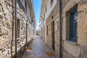 A narrow stone-paved alleyway between buildings with windows and doors, leading to a distant view. - GuestReady - Courtyard 9/99 - Apt 01 (Porto)