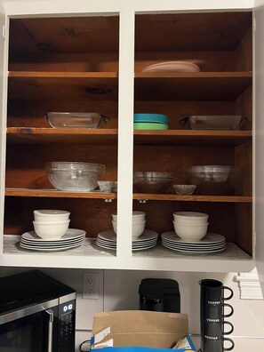 Ein Küchenschrank mit Regalen, auf denen Schüsseln, Teller und eine Kaffeemaschine stehen.