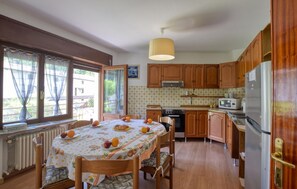 Eine Küche mit Holzausstattung, einem Esstisch mit Obst, einem Heizkörper und einem Fenster mit Vorhängen.