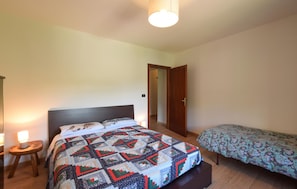 Ein Schlafzimmer mit einem großen Bett, einem kleineren Bett, einem Nachttisch aus Holz und einer Tür zu einem anderen Raum.