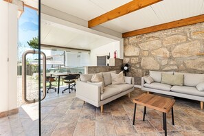 A modern living room with a stone wall, two sofas, a wooden coffee table, and a glass door leading to an outdoor area.
