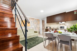 A modern kitchen with a dining area, a staircase, and a stone wall.