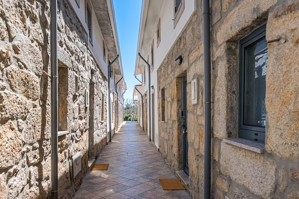 A narrow stone-paved alleyway between buildings with windows and doors, leading to a distant view. - GuestReady - Courtyar 9/99 - Apt 06 (Porto)