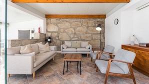 Una sala de estar con pared de piedra, viga de techo de madera, un sofá, una silla, una mesa y una lámpara.