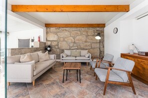 Ein Wohnzimmer mit einer Steinsäule, einem Holzbalken, einer Couch, einem Sessel, einem Tisch und einer Lampe.
