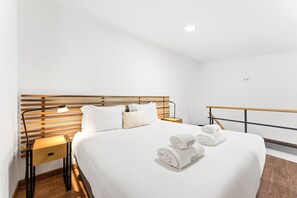 A hotel room with a wooden headboard, a bed with white linens, two bedside tables with lamps, and a rolled towel on the bed. - GuestReady - Courtyar 9/99 - Apt 06 (Porto)