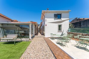 A narrow pathway leading to a white building with a small window and a door, surrounded by outdoor seating and a garden. - GuestReady - Courtyar 9/99 - Apt 06 (Porto)