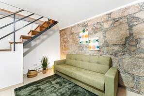 Ein modernes Interieur mit einer Steinwand, einem grünen Sofa, einer Holztreppe und abstrakter Kunst.