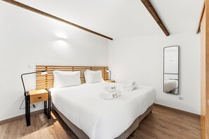 A hotel room with a wooden headboard, a bedside table with a lamp, a large bed with white bedding, and a mirror on the wall. - GuestReady - Courtyar 9/99 - Apt 03 (Porto)