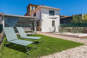 Eine moderne Villa mit Terrasse, zwei Liegestühlen, einem Tisch und einem kleinen Garten.