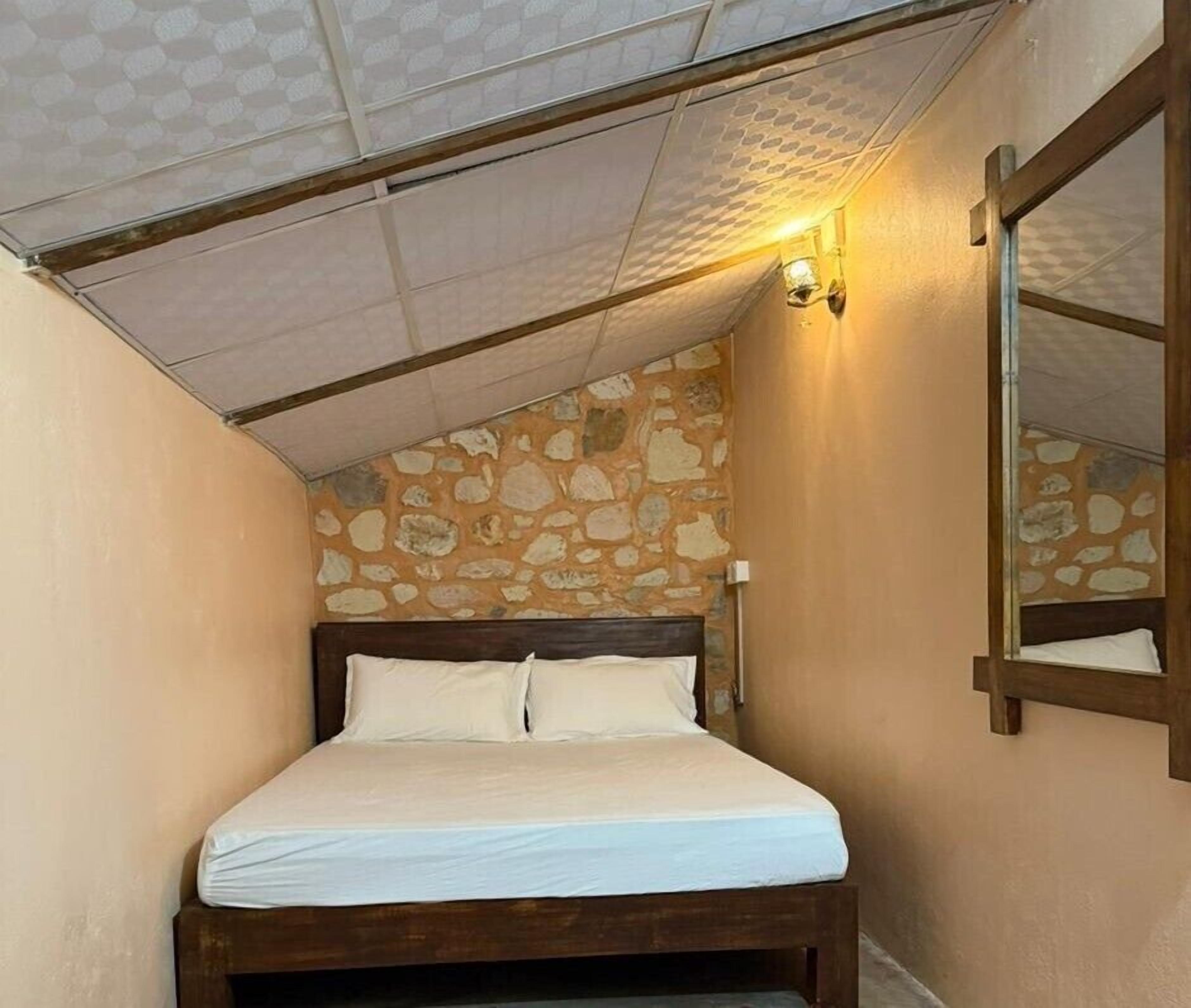 A small, narrow room with a single bed, stone wall, and a slanted ceiling.