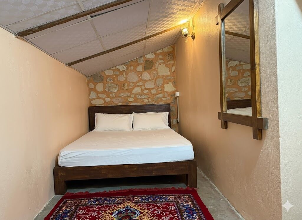 A bedroom with a wooden bed, a red patterned rug, a stone wall, and a ceiling with a skylight.