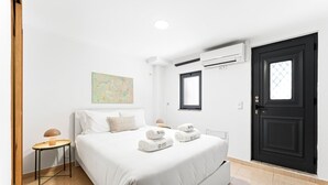 A hotel room with a bed, a bedside table, an air conditioning unit, a door, and a window. - GuestReady - Courtyar 9/99 - Apt 4A (Porto)