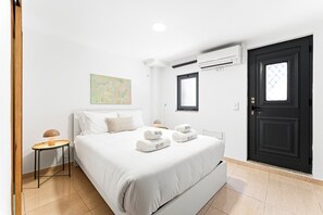 A hotel room with a bed, a bedside table, an air conditioning unit, a door, and a window. - GuestReady - Courtyar 9/99 - Apt 4A (Porto)