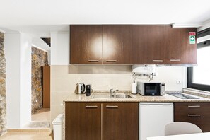 A compact kitchen with dark wooden cabinets, a stainless steel sink, a coffee maker, a microwave, and a dishwasher. - GuestReady - Courtyar 9/99 - Apt 4A (Porto)