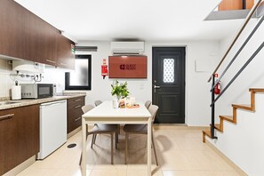 A compact kitchen with a microwave, sink, and cabinets, a dining area with a table and chairs, and a staircase with wooden steps. - GuestReady - Courtyar 9/99 - Apt 4A (Porto)