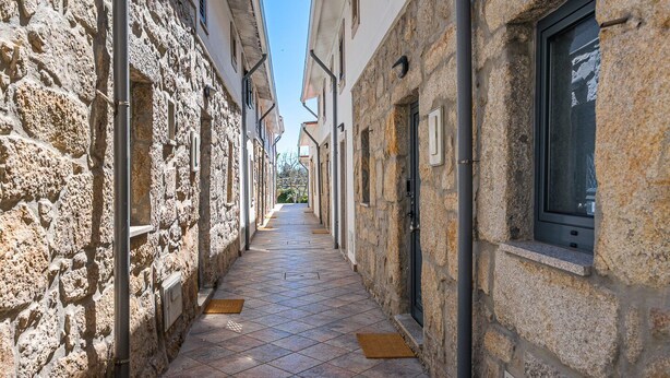 A narrow stone-paved alleyway between buildings with windows and doors, leading to a distant view. - GuestReady - Courtyar 9/99 - Apt 4A (Porto)