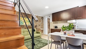 A modern kitchen with wooden cabinets, a dining table with chairs, a green sofa, and a staircase. - GuestReady - Courtyar 9/99 - Apt 4A (Porto)