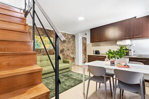 A modern kitchen with wooden cabinets, a dining table with chairs, a green sofa, and a staircase. - GuestReady - Courtyar 9/99 - Apt 4A (Porto)