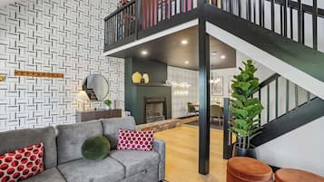 A modern living room with a grey sofa, a staircase, and a patterned wall.