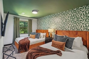 Une chambre d’hôtel avec deux lits, une télévision, une fenêtre avec des rideaux, un mur à motifs et une table de chevet avec une lampe.