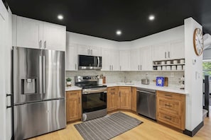 Une cuisine moderne dotée d’appareils électroménagers en acier inoxydable, de meubles en bois et d’un plafond noir.