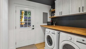 Un lavadero con lavadora, secadora y una puerta que da a un balcón con un paraguas amarillo.