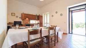 A dining area with a table set for four, wooden chairs, a kitchen in the background, and a sliding glass door leading outside. - Awesome apartment in Castellabate (Castellabate)