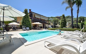 A swimming pool with lounge chairs, umbrellas, and a building with a balcony in the background. - Awesome apartment in Castellabate (Castellabate)