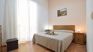 A bedroom with a bed, a nightstand, a lamp, a painting on the wall, and a window with curtains. - Awesome apartment in Castellabate (Castellabate)