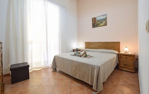 A bedroom with a bed, a nightstand, a lamp, a painting on the wall, and a window with curtains. - Awesome apartment in Castellabate (Castellabate)