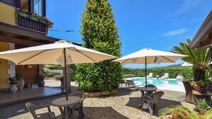 A patio area with stone flooring, outdoor seating, umbrellas, a pool, and a tall green hedge. - Awesome apartment in Castellabate (Castellabate)