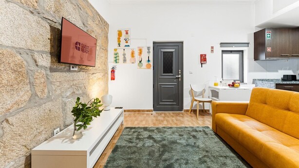Ein modernes Wohnzimmer mit Steinwand, Flachbildfernseher, einer Couch, einem Couchtisch und einer Küchenzeile mit Schränken und einem Fenster.