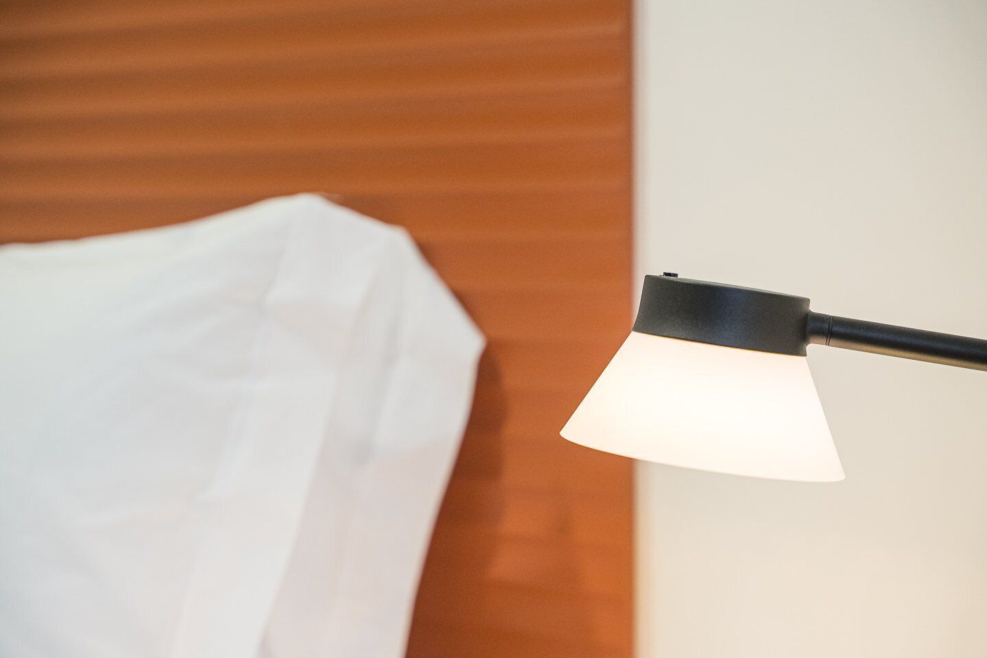 A bed with a white sheet and a black lamp with a white shade.