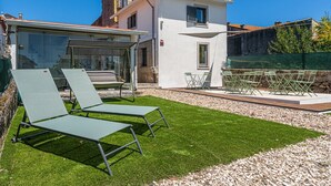 Eine moderne Villa mit Terrasse, zwei Liegestühlen, einem Tisch und einem kleinen Garten.