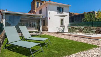 Eine moderne Villa mit Terrasse, zwei Liegestühlen, einem Tisch und einem kleinen Garten.