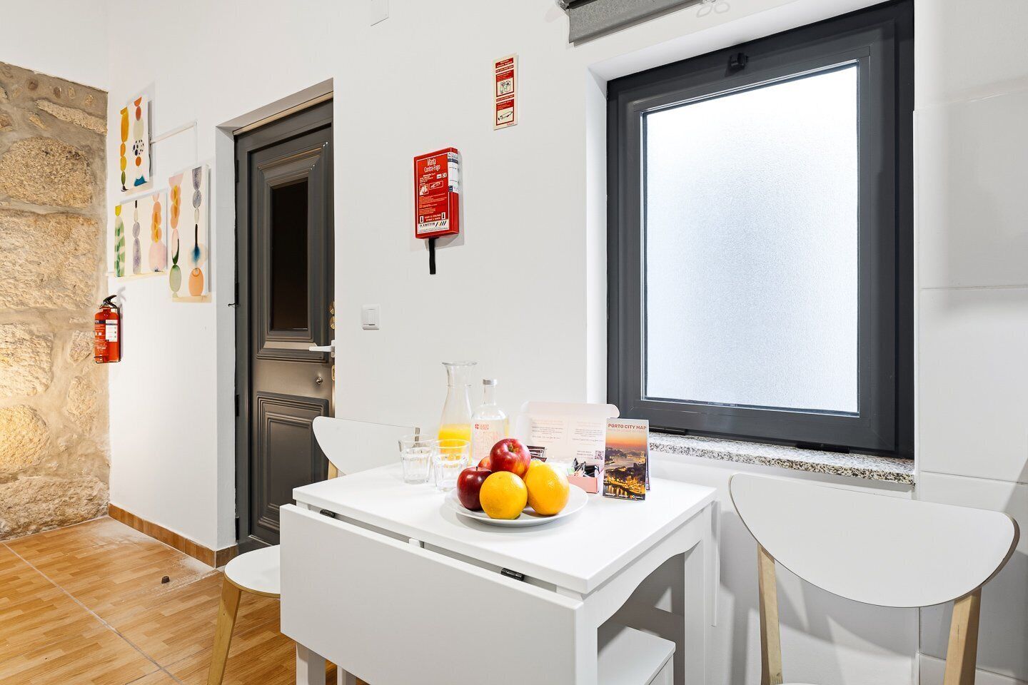 Eine moderne Küche mit weißen Schränken, einem Esstisch mit Stühlen, einem Fenster mit Aussicht und einem Feuerlöscher an der Wand.