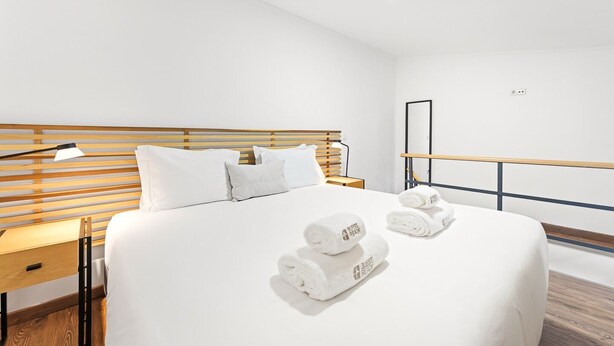Ett hotellrum med en sänggavel i trä, en säng med vita sängkläder, två sängbord med lampor och en uppsättning handdukar på sängen.