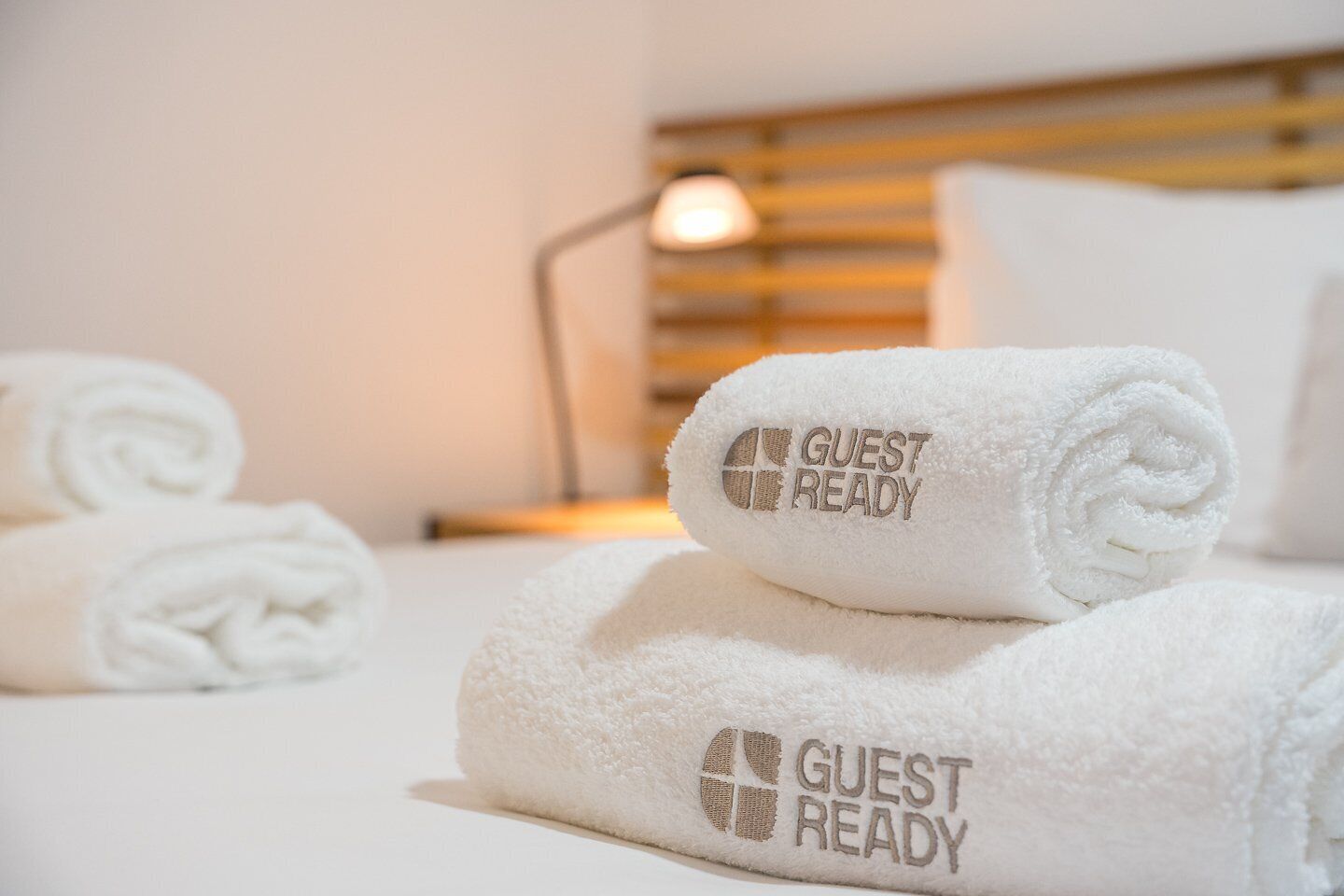 Cama arrumada com toalhas brancas dobradas e um aviso com a inscrição 'GUEST READY'.
