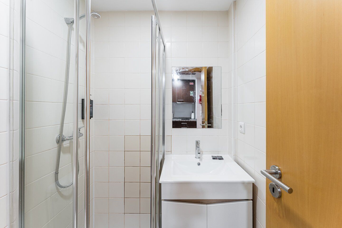 A bathroom with a glass shower enclosure, a sink, and a mirror.