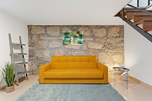 Ein Zimmer mit einer Steinswand, einem gelben Sofa, einem kleinen runden Tisch und einer Treppe.