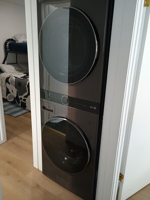 Ein kompakter, moderner Raum mit integriertem Waschtrockner, einem Bett mit gemustertem Überwurf und einem kleinen Teppich auf dem Boden.