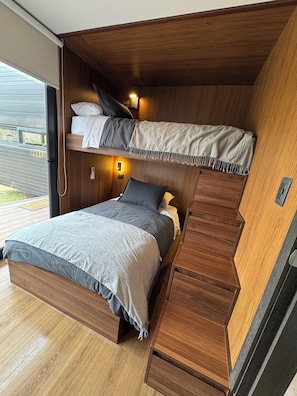 A bunk bed with a wooden headboard, a bedside table, and a wall-mounted light.